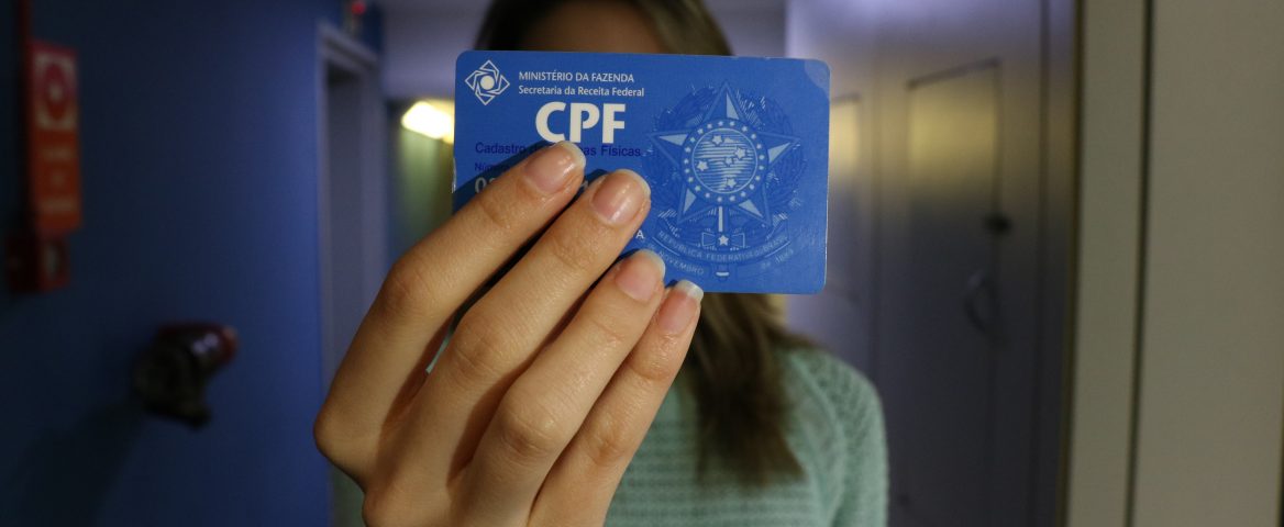Uma jovem segura o cartão de CPF em frente ao rosto.