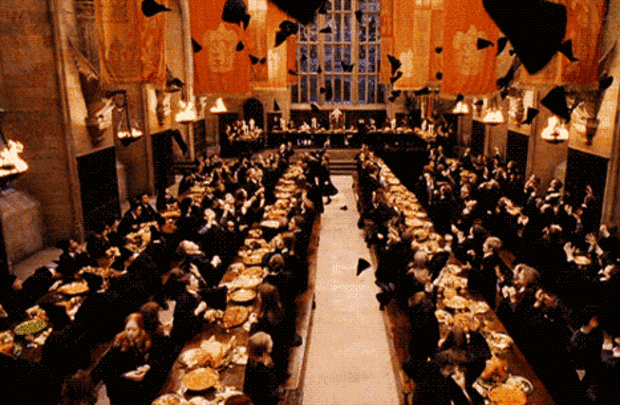 O salão comunal de Hogwarts. Há quatro mesas compridas com muitos alunos em volta delas. Um banquete está sendo servido. Há bandeiras vermelhas da Grifinória penduradas. Todos os alunos, menos os da Sonserina, jogam seus chapéus para o alto. 