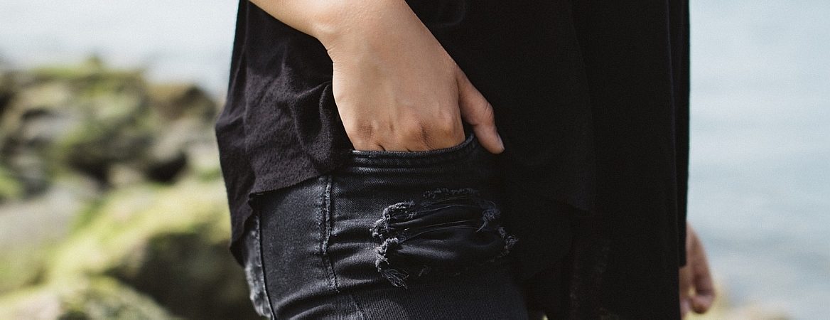 Adolescente anda na praia com a mão no bolso. Ela veste jeans e camiseta preta