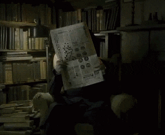 Em uma sala com livros, um homem está sentado lendo um jornal. Sua face está encoberta. Ele, então, deixa o jornal dobrar revelando sua face. É o professor Snape com expressão de cara fechada. 